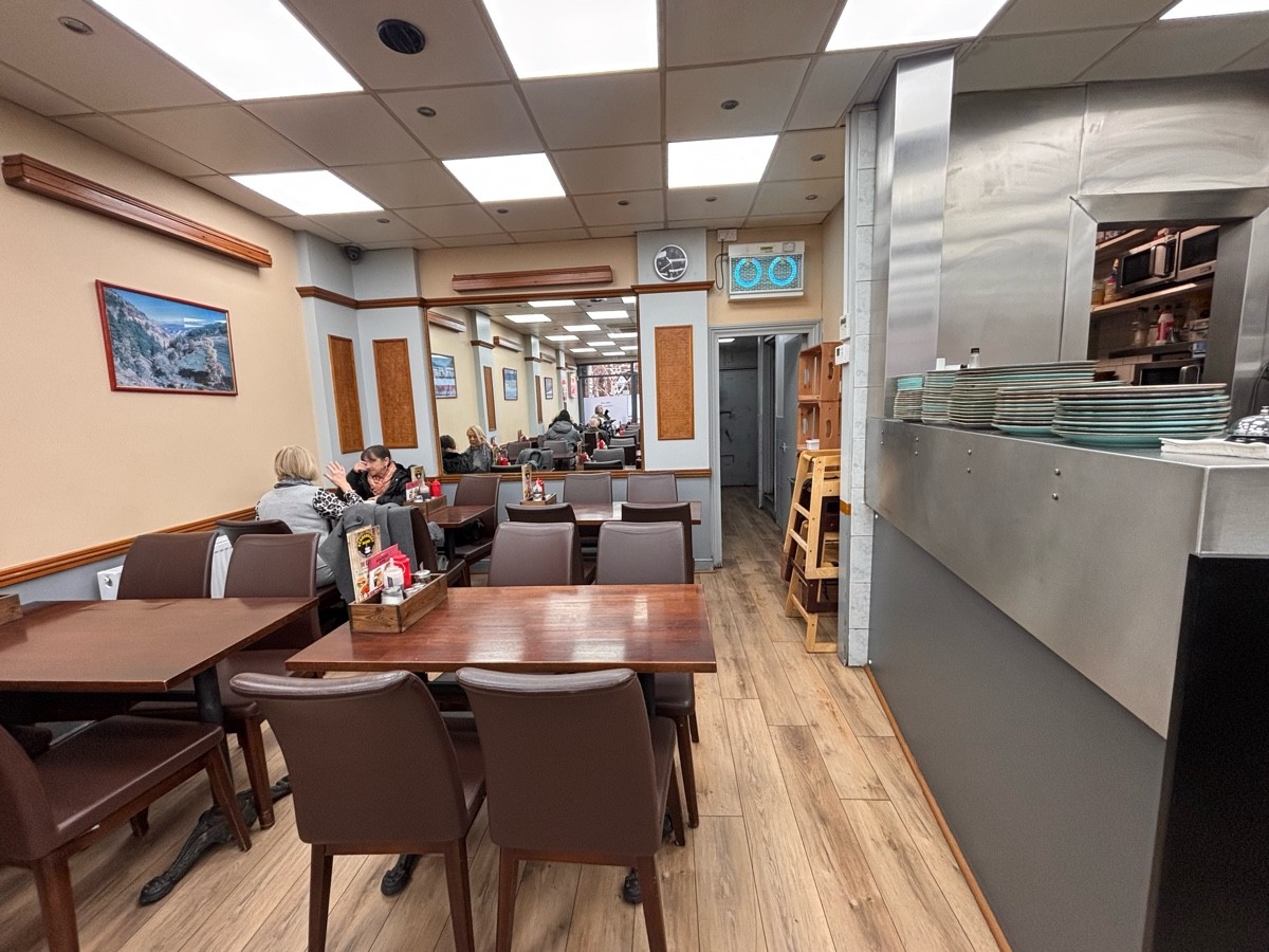 From end of counter facing straight. Tables and chairs along left. Kitchen counter along right.