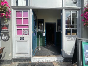 From pathway looking at main entrance. One step up. Blue and glass double doors. Push in the centre.