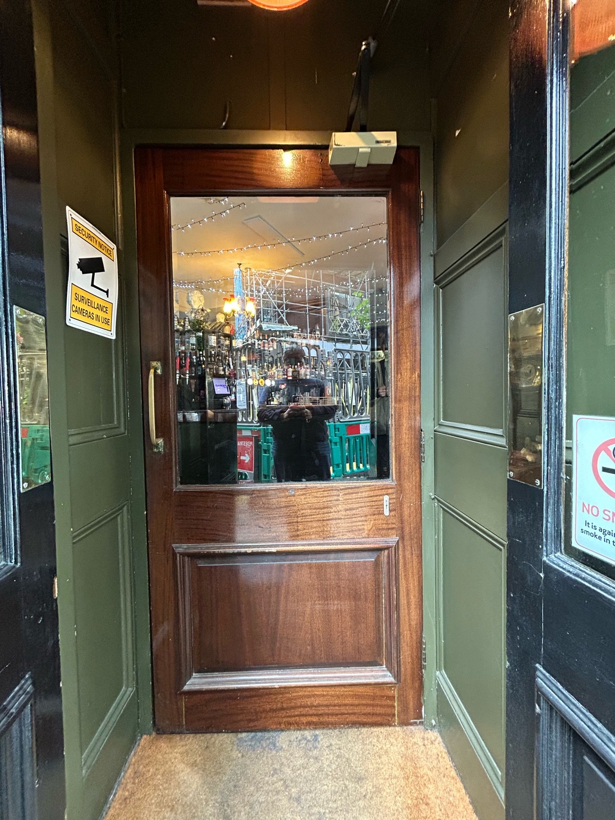 From preceding door facing straight. Brown wooden door with glass panel. Gold vertical handle on left, pull to open.