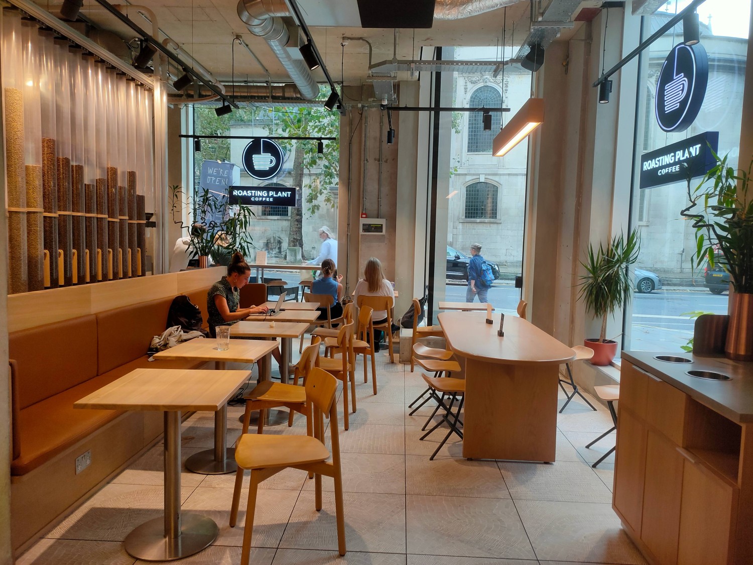 From back left of main area, facing left. Half booth along left. Table with stools at back right. Condiment station on right. Tables at far back.