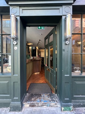 Single dark green wooden door with glass panels and gold vertical metal handle along left. Push to open.