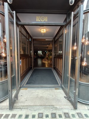 Facing double glass entrance doors. Pull vertical metal handles in centre to open.