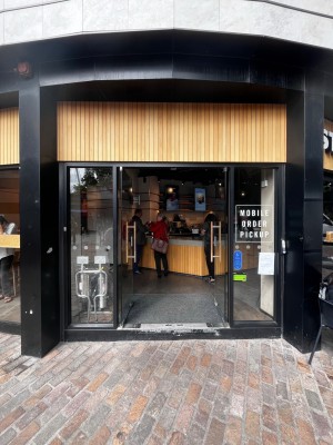 Double glass doors with brown handles. Step at entrance followed by small bump. Doorbell for assistance to the right. Push to open.
