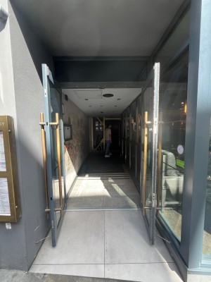 Grey framed glass doors ahead. Pull open via long gold handles in centre. Pathway after door.