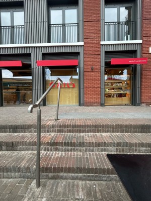 From back of outdoor area tables facing straight. Steps up to top of ramp. Silver handrail on left.