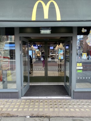 Directly facing the entrance of the MacDonalds from the street. Two sets of wide double glass doors. The first door is are manual doors that have been propped open. The second doors behind are automatic sliding doors.