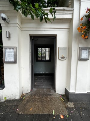 Built in ramp leading to preceding door. Grey wooden door. Push from right to open.