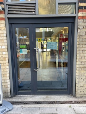 Glass door with grey, metal frame. Pull silver handle on left to open.