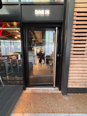 Glass door with black doorframe ahead. Push metal handle at center right of door to open.