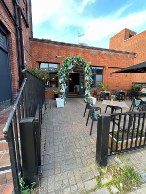 From side street. Push black gate opening form right. Pathway ahead through flower archway.