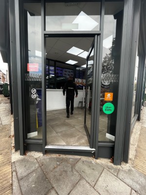 Glass door with grey frame. One step up through door. Push from left to open.