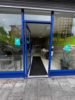 Glass door with blue frame. Push from right to open. Small step up through door.