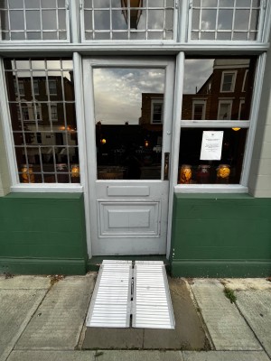 Glass door with grey wooden frame ahead. Push metal handle at center right to open. Ramp up one request.