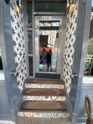 Three steps up with silver handrails on both sides to door. Grey framed glass door. Push from left to open.
