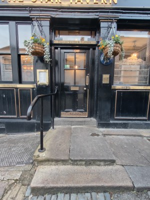 Facing entrance. Black framed glass door. Push golden handle on right to open. Two steps up before door with black metal handrail on left.
