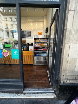 Glass door with black frame. Push from left to open. Two very small steps up through door.