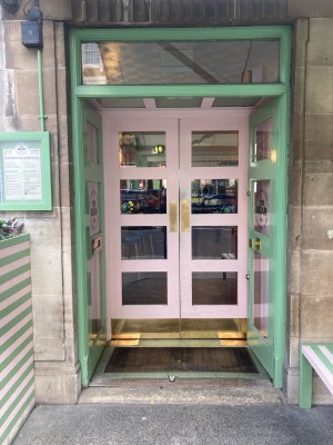 Glass doors with turquoise frame ahead. Push from center to open.