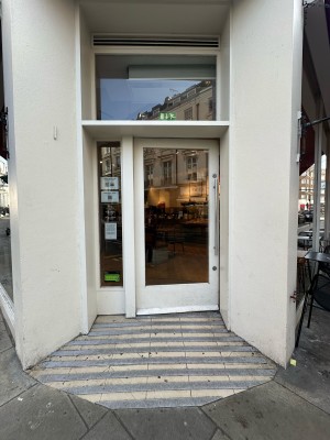 Glass door with white frame ahead. Pull from metal handle on right to open.