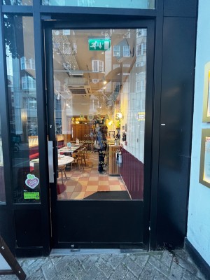 Glass door with black metal frame. Push from left to open.