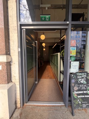 Glass door with grey doorframe ahead. Push metal handle at center right to open.