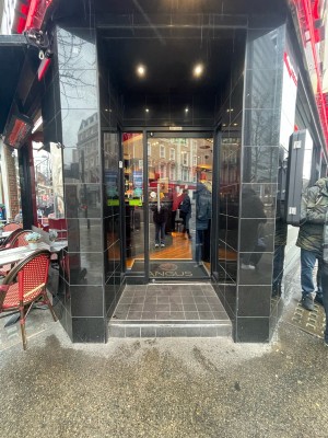 Glass door with black frame. Step up ahead of entrance. Pull handle on left to open.