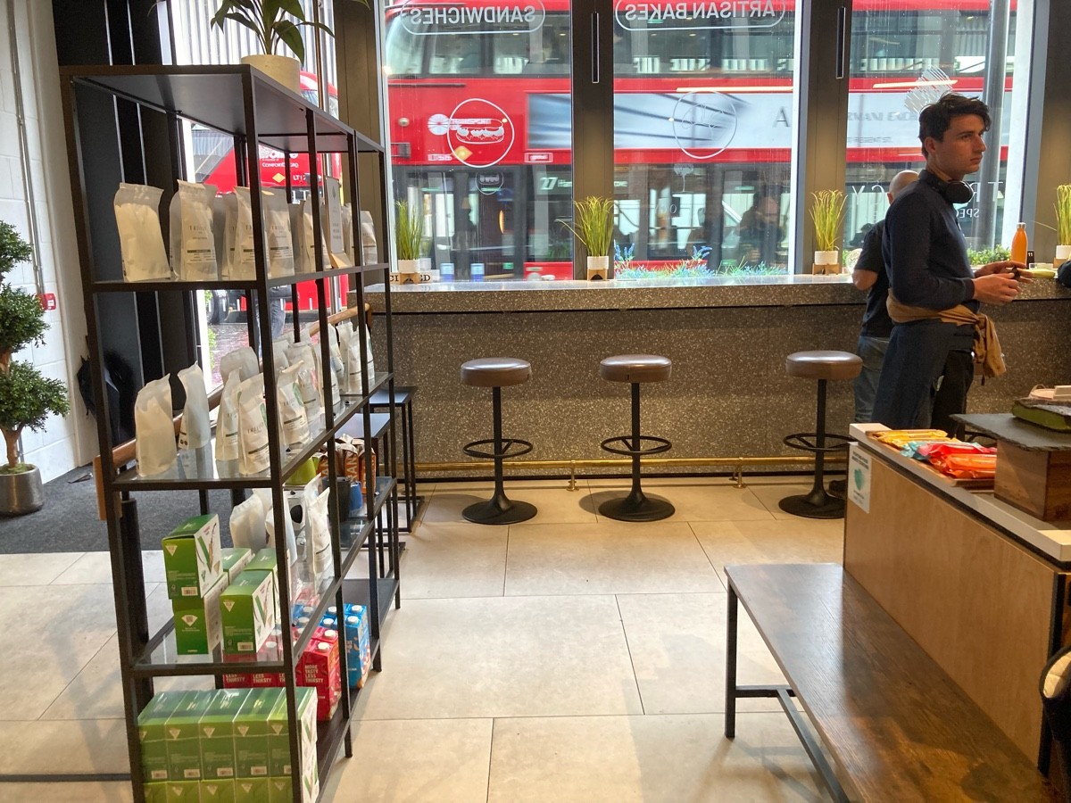 From shelve facing left. Bench along right. Product shelves along left. High table and stools along back.
