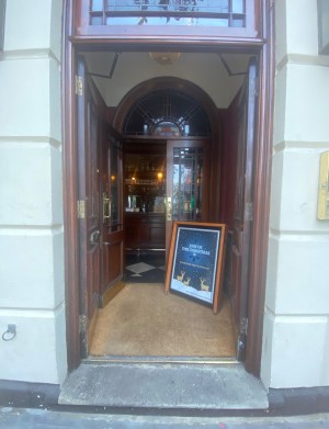 Glass double doors with wooden frames straight ahead. Push from middle to open. 1 step before doorway.