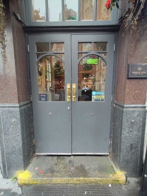 Grey doors with glass panels ahead. One step up before door. Pull doors to open in centre via handles.