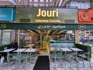 Black carpet on central path with outdoor seating area on either side. Main entrance straight ahead. Glass door with handle on right. Push to open.