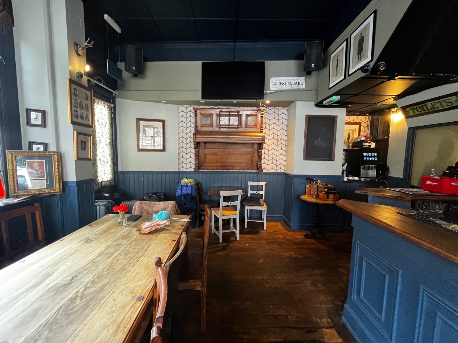 Continuing facing ahead from path. Table with chairs on back wall ahead. Bathroom staircase on right wall after bar.