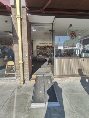 Ramp on request to glass door ahead. Push silver handle on left to open. Silver handrail on left of ramp. Doorbell for assistance on left of door.