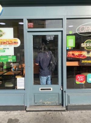 Single glass door, with grey doorframe. Push door open from the right.