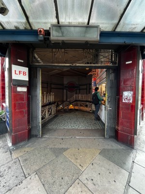 Tube station entrance. Wide open archway. Kiosk on immediate right wall through archway.
