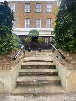 From street facing venue. Steps straight ahead. Hand rail on both sides. Path after steps leads straight through outdoor seating area to door.