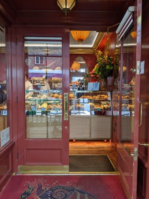 Glass doors with red frame and metal handle in centre. Pull to open. Built-in ramp covered by doormat before doors.