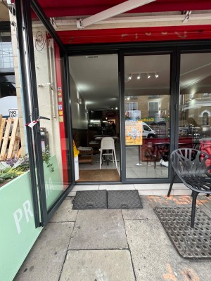 Glass door with metal frame. Pull to open with handle on right hand side. Small bump at foot of door. One step to door. Ramp available upon request.