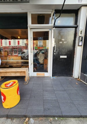 From sidewalk, looking straight ahead. Step from sidewalk leading to main door straight ahead. Glass door with white border. Push from left to open.