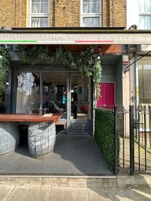Opening ahead with outdoor seating on right. Glass door with grey frame ahead. Push silver handle on left to open.