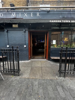 From pavement facing venue. Fence on left and right. Built-in ramp ahead followed by entrance.