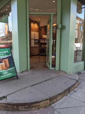 Glass door with green frame and metal handle on left. Push to open.