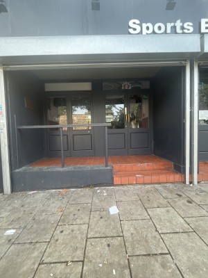 Door on the right side of the venue with steps in front. Small handrail to the left of the steps. Door with dark grey frame.