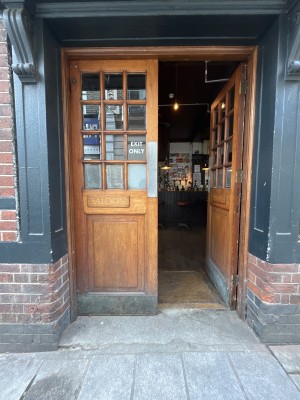 From right of main entrance facing straight. Wood doors with glass panels and metal handles ahead. Push from centre to open.