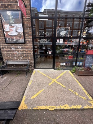 Ramp up to glass door with black frame and metal handle. Push from right to open.