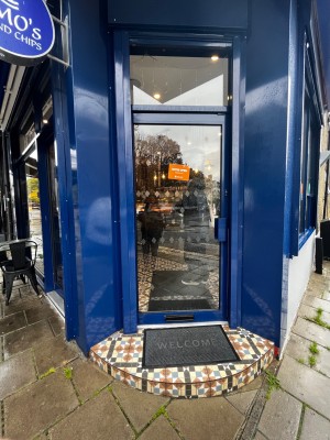 Glass door with blue frame. Push from right to open. One step up to door followed by small bump at foot of door.