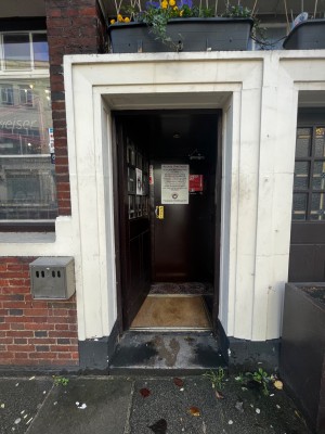 Dark brown wooden door. Push from right to open. One step up through door.