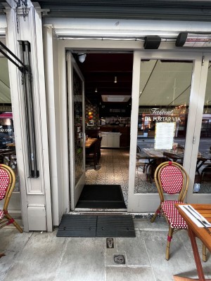 Grey framed glass door. Push silver handle on right to open. Portable ramp going up before door and going down after door.