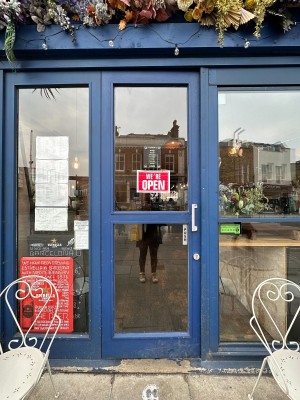 Glass door with blue frame and metal handle on right. Push to open.