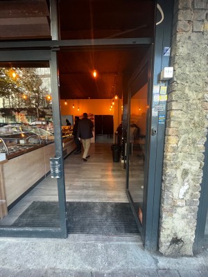 Glass double door with grey frame. Push right door from left to open. Built in ramp up to door followed by small bump at foot of door.