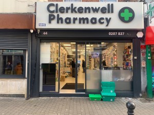 Main entrance to the pharmacy, taken from the opposite side of the street. The interior is visible through the glass front and the sliding door.