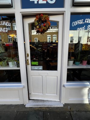 Glass wall with white frame. Push from left to open. One step up through door.